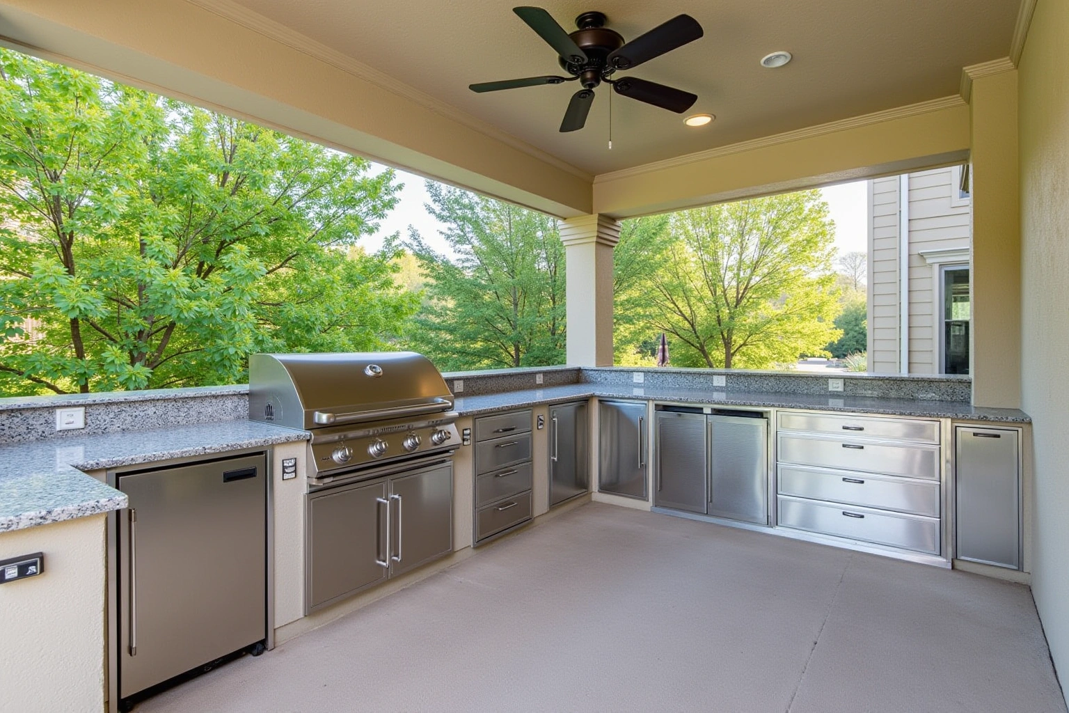 Covered patio kitchen with stainless doors and drawers under a speckled granite counter, a built-in grill and ceiling fan.